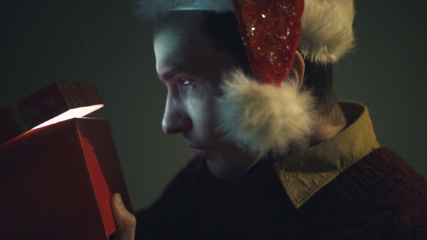 Close up of surprised man opening luminous gift box at night Christmas Eve time - Filmagem, Vídeo