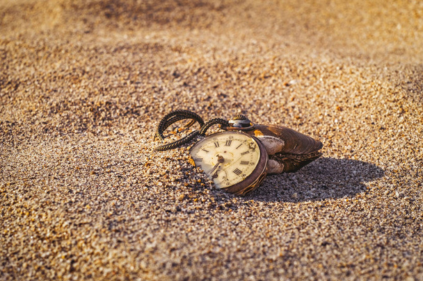 Nature morte - Montre de poche antique pourrie enterrée partiellement dans le sable
 - Photo, image