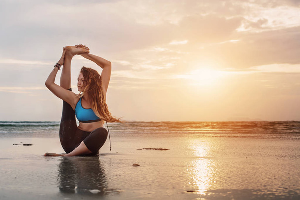 Young woman practicing yoga on the beach at sunset - Foto, imagen