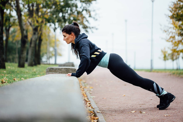 Portrait of woman in sportswear, doing fitness push-ups exercise at fall park, outdoor. - Фото, зображення