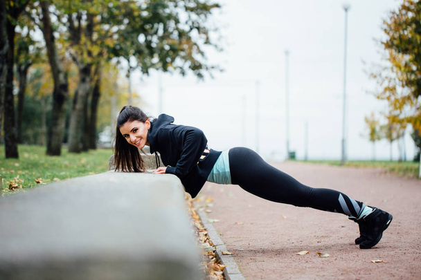 Portrait of woman in sportswear, doing fitness push-ups exercise at fall park, outdoor. - Photo, Image