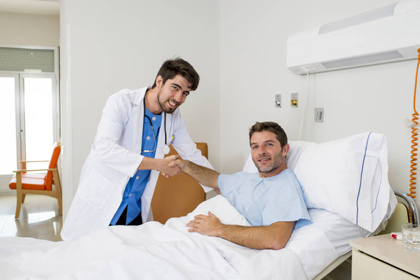 lekarz konsultacji pacjenta leżącego na łóżku szpitalnym, trwający zwolniony drżenie rąk w nowoczesnej kliniki - Zdjęcie, obraz