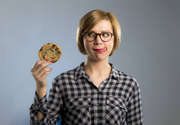 νεαρή ξανθιά χαριτωμένα και φιλικό καυκάσιος γυναίκα στο casual ρούχα κρατώντας μεγάλο γευστικό μπισκότο σοκολάτας  - Φωτογραφία, εικόνα