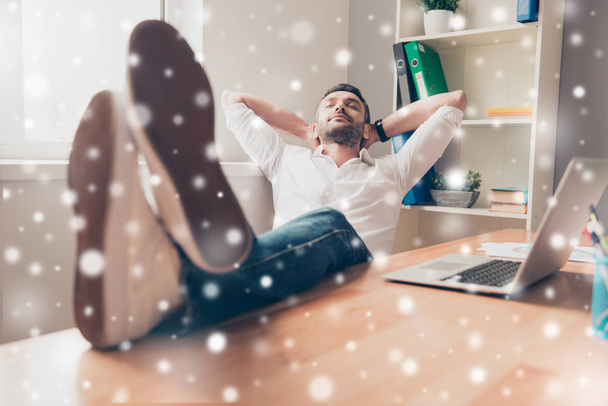 Relaxed happy man  holding legs on table on snowy background - Foto, immagini