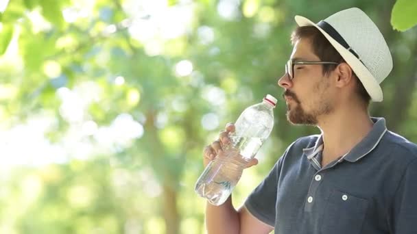 Thirsty man drinking water from bottle in summer park. Portrait of sport man drinking mineral water after outdoor workout. Runner training in city park - Footage, Video