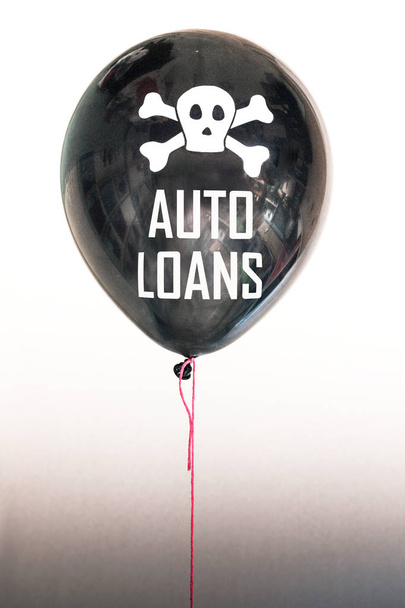 die Worte Autokredite in Weiß und ein Totenkopf und Kreuzknochen auf einem Luftballon, die das Konzept einer Schuldenblase illustrieren - Foto, Bild