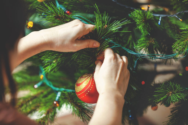 Decorate the Christmas tree. Woman's hand hangs a beautiful toy red ball on green coniferous branch close-u - Photo, Image
