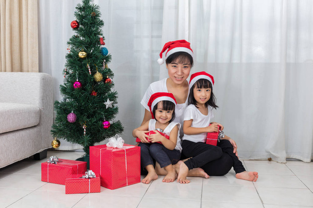 Asian Chinese mother and daughters sitting next to Christmas tre - 写真・画像