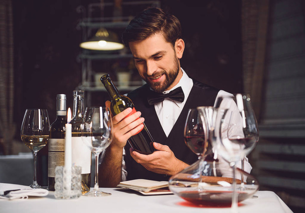 Wine critic holding bottle of scarlet drink with smile - Foto, afbeelding