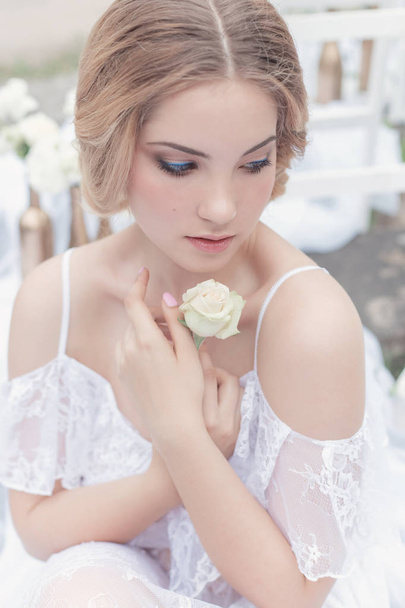 beautiful young sweet blonde girl with a wedding bouquet in the hands of the boudoir in a white dress with evening hairstyle walks near the ruins - Foto, Bild