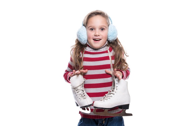 Lovely smiling little girl wearing colorful striped sweater and headdress, holding skates isolated on white background. Winter clothes. - Fotoğraf, Görsel