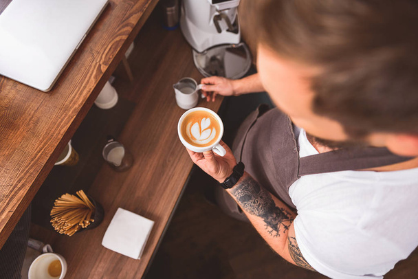 coffeemaker holding mug with latte art - Foto, afbeelding