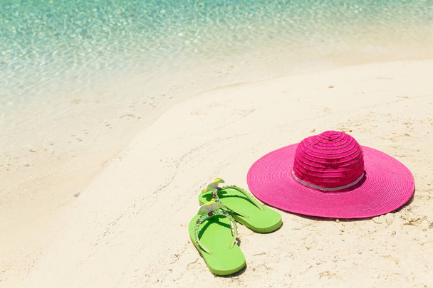 Ροζ καπέλο και τα πράσινα παντόφλες παραλία στη χρυσή άμμο από θάλασσα shor - Φωτογραφία, εικόνα