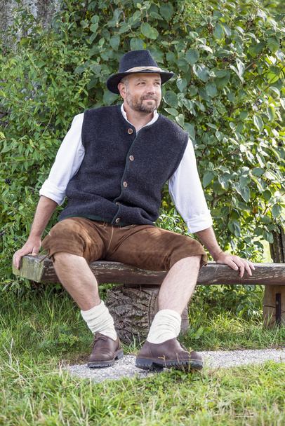 Seated man in traditional Bavarian costumes and black hat - Foto, Bild