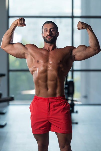 Kehonrakentaja suorittaa edessä Double Biceps Pose kuntosalilla
 - Valokuva, kuva
