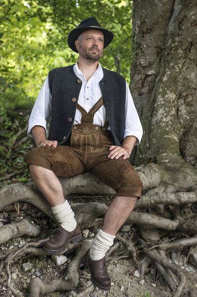 Seated man in traditional Bavarian costumes in forest - Foto, Imagen