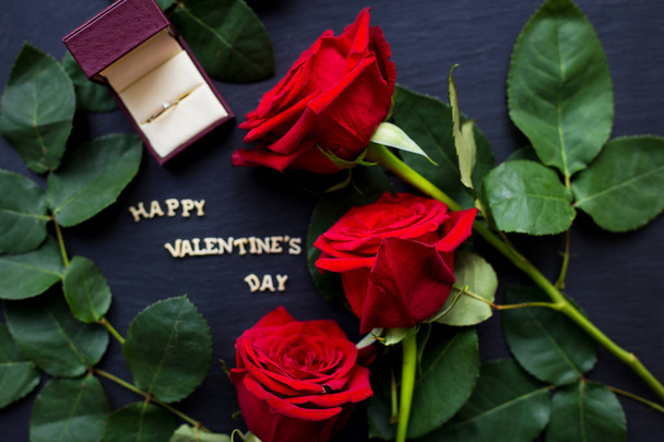 die Inschrift "happy valentine" auf schwarzem Hintergrund mit roten Rosen und Ehering - Foto, Bild