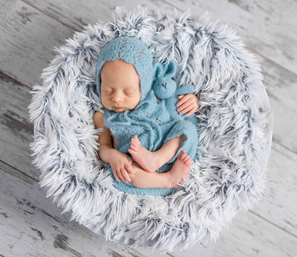 lovely infant in hat and jumpsuit sleeping on round bed - Фото, изображение