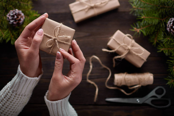 Beautiful female hands are packed Christmas gift in brown kraft paper. - Foto, immagini