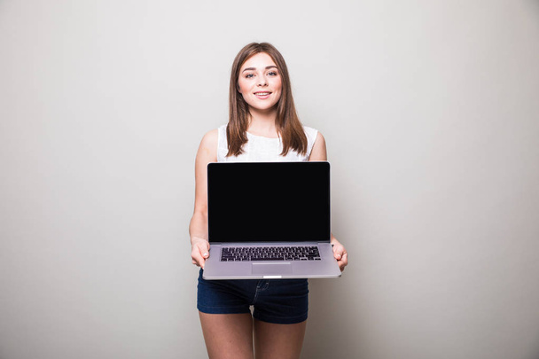 κορίτσι στέκεται και χρησιμοποιώντας το laptop πάνω από το γκρίζο φόντο - Φωτογραφία, εικόνα