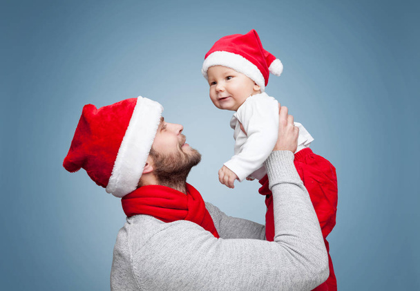 Father with baby boy wearing Santa hats celebrating Christmas - Photo, Image