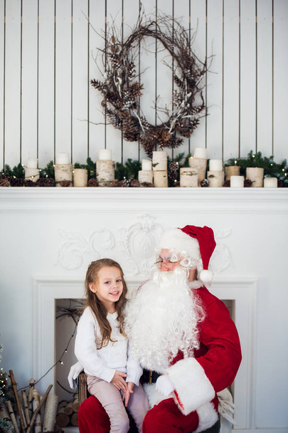 el sueño es real en Navidad. feliz niña linda sentada en el regazo de edad Santa Claus y abrazos en casa cerca del árbol de Navidad
 - Foto, Imagen
