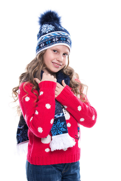 Pretty smiling little girl with curly hairstyle wearing knitted sweater, scarf and hat with skates isolated on white background. Winter clothes and sport concept. - Photo, Image