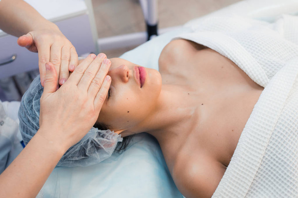 Улыбающаяся брюнетка наслаждается массажем головы в спа-салоне
 - Фото, изображение