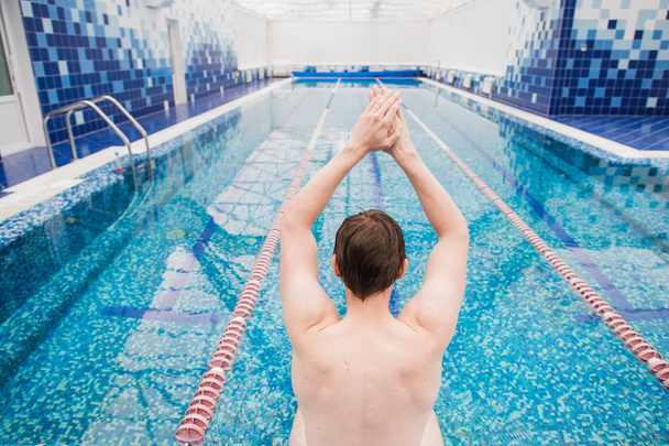 Спортивный активный образ жизни. Спортивный мужчина мужской пловец мускулистое тело готовится прыгать и нырять в бассейн задний вид
 - Фото, изображение