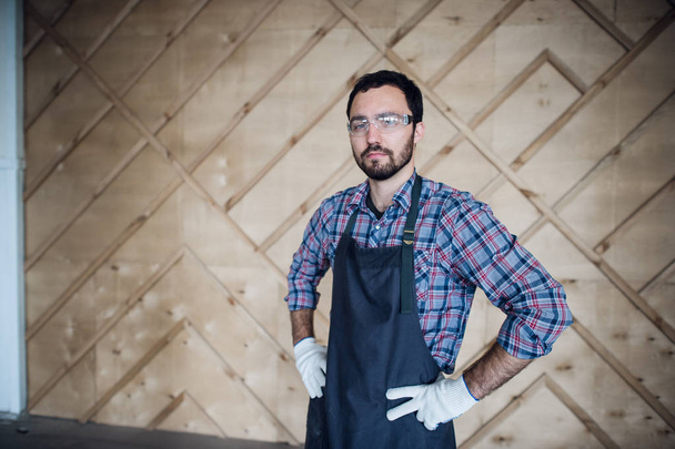 Young male carpenter wearing gloves and glasses with hands on hips - Foto, afbeelding