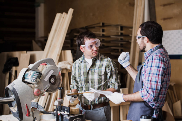 Tarkastaja ja puuseppä keskustelevat puutuotteiden valmistusprosessista huonekaluille
 - Valokuva, kuva