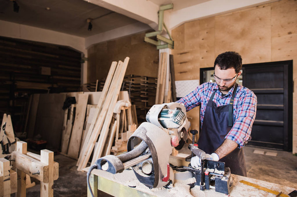 Плотник с помощью циркулярной пилы для древесины в своей мастерской
 - Фото, изображение
