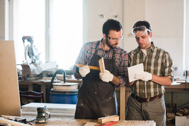 Heureux charpentier masculin montrant quelque chose à collègue à ses papiers de cahier dans l'atelier
 - Photo, image