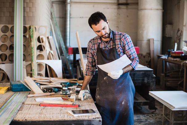 Portrait of a carpenter standing in his woodwork studio and holding notebook - Photo, Image