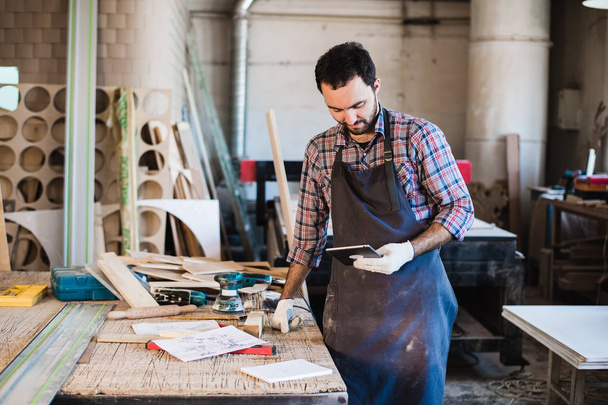 Portrait of a carpenter standing in his woodwork studio and holding digital tablet - Photo, Image