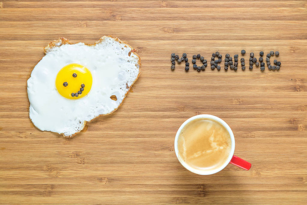 Smiling fried egg lying on a white plate on a wooden cutting board with silver fork near it. Classic Breakfast concept. - Photo, image