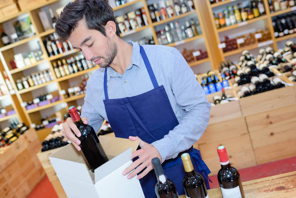 seller wearing apron preparing box with bottles in wine store - Zdjęcie, obraz