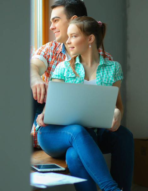 Portrait of young couple moving in new home sitting with laptop - Foto, afbeelding