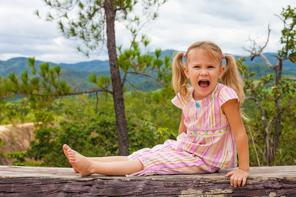 Happy child sits on a log in the background of mountains - Foto, Bild