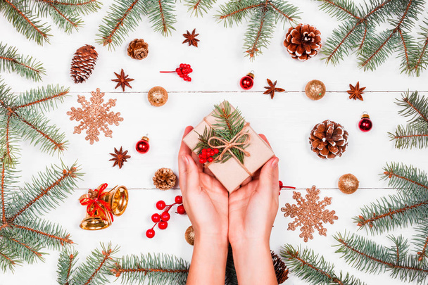 Christmas background with fir branches, pine cones, skein of jute, red decorations. Female hands holding Christmas gift. Xmas and Happy New Year composition. Flat lay, top view - Фото, зображення