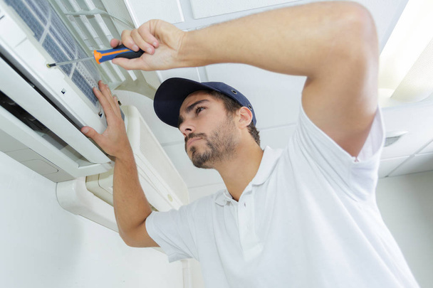 portrait of mid-adult male technician repairing air conditioner - Fotó, kép