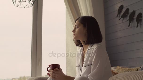 Привлекательная девушка смотрит в окно на уютную квартиру
. - Кадры, видео