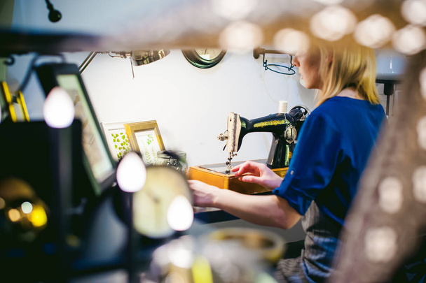 seamstress work on the sewing machine. young blonde woman working on a mechanical sewing machine at home sitting at your desk, be prepared to sew - Foto, Bild