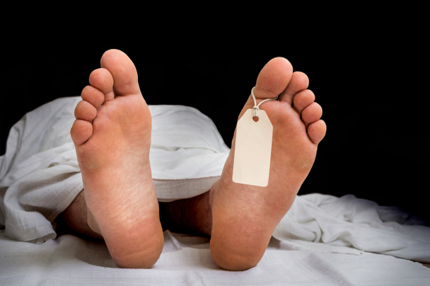 Kuolleen miehen ruumis, jossa on tyhjä lappu jaloissa valkoisen kankaan alla.
 - Valokuva, kuva