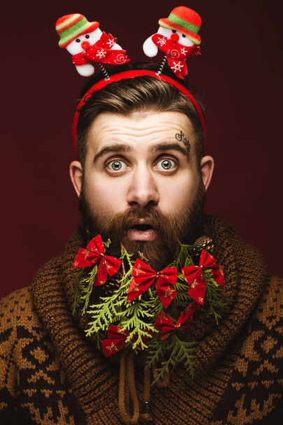 Hombre barbudo divertido en una imagen de Año Nuevo como Santa Claus con decoraciones en su barba. Fiesta de Navidad
. - Foto, Imagen