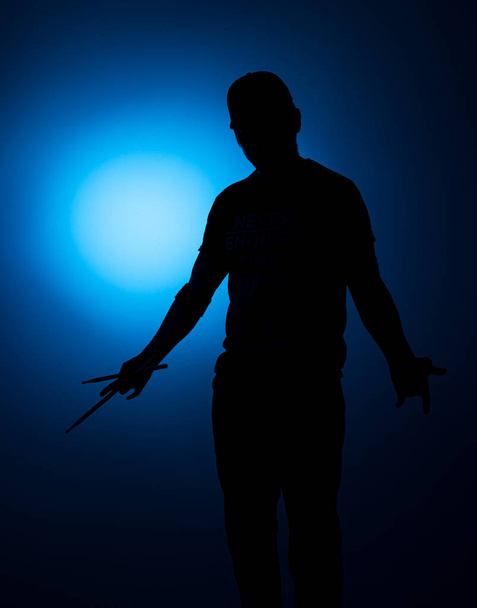 silhouette Expressive young drummer with drum stick on a blue background - Zdjęcie, obraz