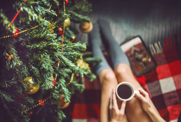Feet girl in socks with a cup in hand and dressed up Christmas tree - Photo, image
