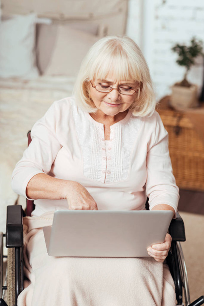 Pleasant elderly woman using laptop in the wheelchair - 写真・画像