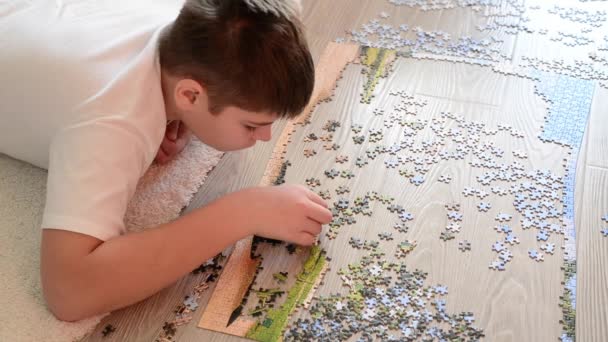 Teen boy collects a puzzle lying on floor - Video