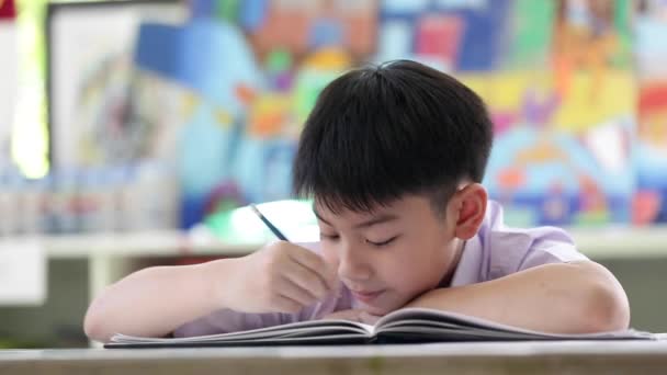 Niño asiático en uniforme de estudiante leyendo y escribiendo para hacer la tarea de la escuela
 . - Metraje, vídeo